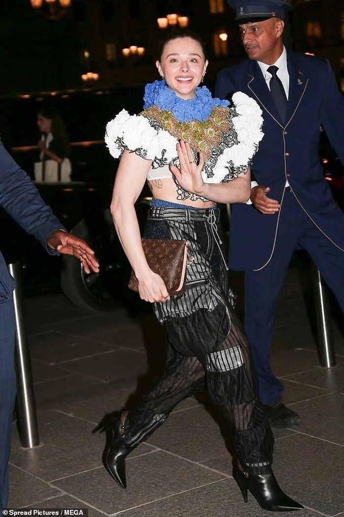 Chloe Grace Moretz diện áo crop top bèo nhún trắng - xanh với nhiều lớp chất liệu, kết hợp quần da đen dáng rộng và boots cao gót. Thiết kế ngắn để lộ phần eo cùng một hình xăm ít khi xuất hiện trước công chúng của cô. Trước show một ngày, Moretz cũng dự tiệc riêng của thương hiệu tại Paris. Ảnh: shutterstock, MEGA.