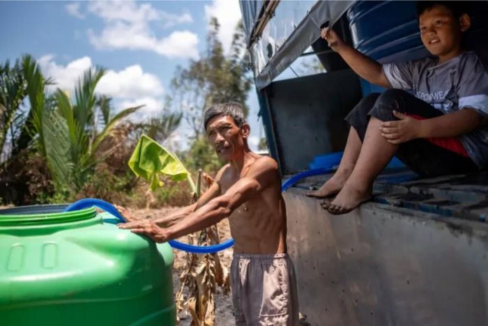 Ông Võ Thanh Thuận và con trai lấy nước sạch do các nhà hảo tâm từ những tỉnh lân cận mang đến để đổ đầy bồn nhựa tại huyện Tân Phú Đông, tỉnh Tiền Giang, Việt Nam - Ảnh: Linh Phạm