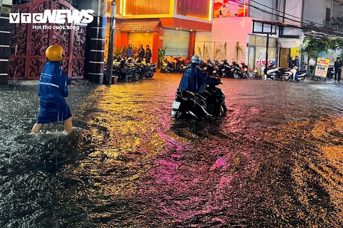 Nhiều người mặc áo mưa cố gắng chạy xe qua khu vực ngập. Một số xe bị chết máy giữa đường, người dân phải xuống xe, bì bõm lội nước và dắt phương tiện vào khu vực cao hơn.