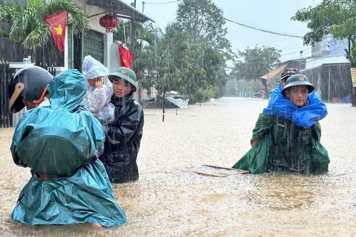 Lực lượng chức năng đội mưa hỗ trợ người dân ở xã Núi Thành sơ tán khỏi khu vực ngập sâu. Ảnh: Quang Cường