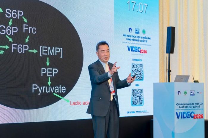 GS. Akira Hamura minh họa quá trình vi khuẩn khoang miệng chuyển hóa đường thông thường thành axit lactic phá hủy men răng tại VIDEC 2026