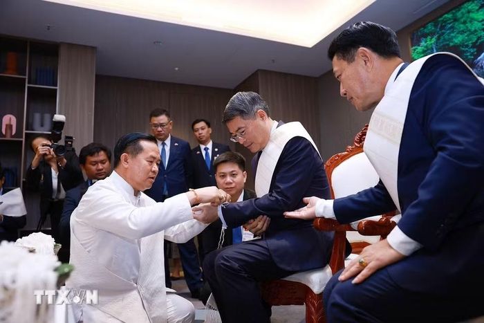 Thủ tướng Lê Minh Hưng thực hiện nghi thức buộc chỉ cổ tay truyền thống của Lào. (Ảnh: Dương Giang/TTXVN)
