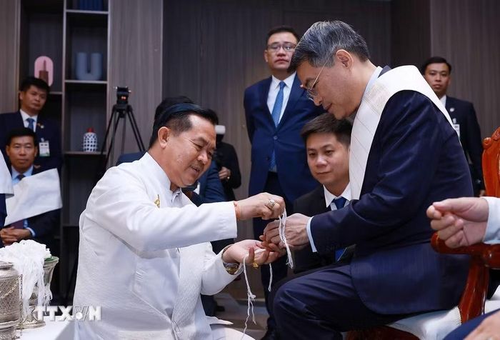 Thủ tướng Lê Minh Hưng thực hiện nghi thức buộc chỉ cổ tay truyền thống của Lào. (Ảnh: Dương Giang/TTXVN)