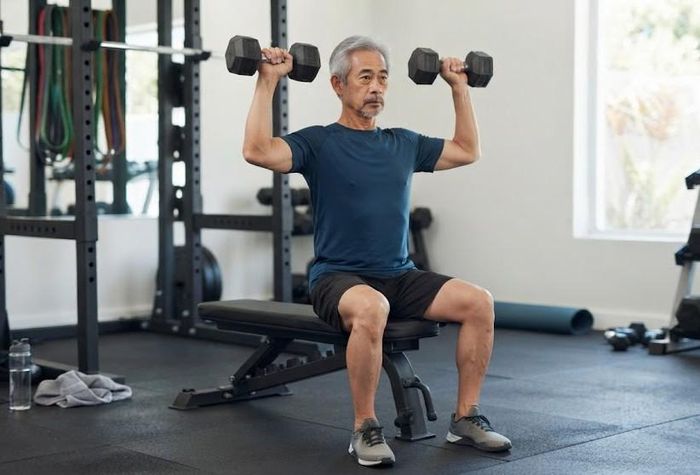 Đẩy tạ qua đầu khi ngồi giúp tăng sức mạnh vai. Ảnh: AI.