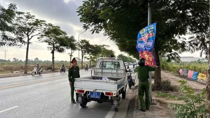 Cán bộ, chiến sĩ Công an xã Thanh Trì tháo gỡ băng rôn quảng cáo treo sai quy định trên cột điện ven đường