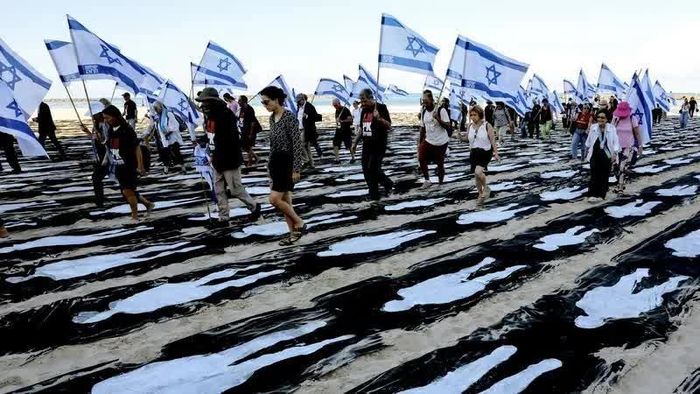 Người dân Israel cầm cờ đi qua một công trình tưởng niệm được dựng trên bãi biển ở Tel Aviv. (Nguồn: Getty Images)