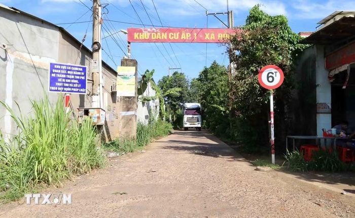 Xe tải lưu thông qua lối vào khu dân cư ấp Đồng Tiến, nơi có biển cảnh báo ghi hình, truy thu và xử lý các hành vi né tránh trạm thu phí. (Ảnh: Đậu Tất Thành/TTXVN)