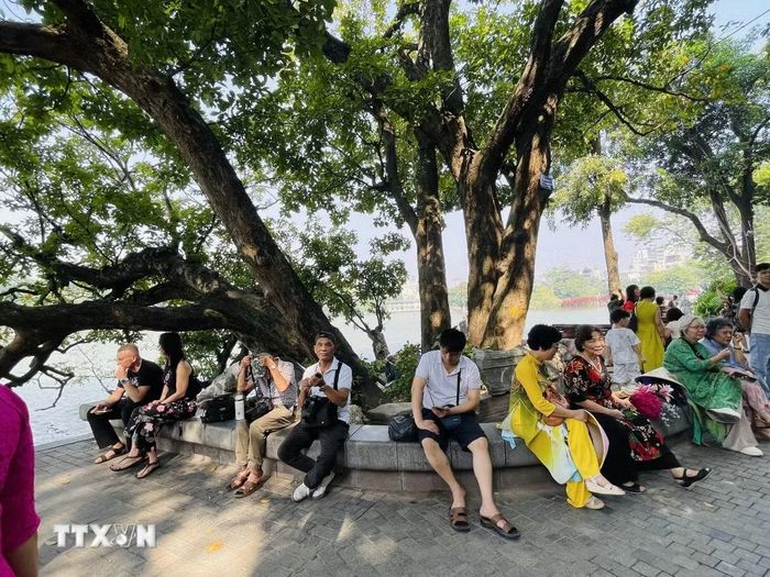 Người dân và du khách nghỉ chân bên gốc cây cổ thụ ven hồ Hoàn Kiếm để cảm nhận không khí dễ chịu của mùa Thu Hà Nội. (Ảnh: Tuyết Mai/TTXVN)