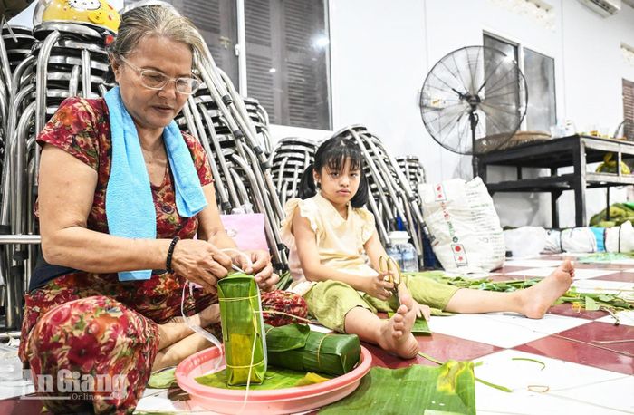 Bà Trần Thị Hoàng Mai (69 tuổi) ngụ phường Rạch Giá cùng cháu nội gói bánh tét phục vụ lễ hội.