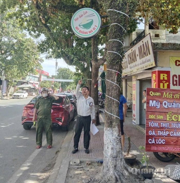 Anh Lý Quang Hào cùng lực lượng chức năng kiểm tra, hướng dẫn người dân treo biển hiệu đúng quy định, bảo đảm trật tự hành lang an toàn giao thông - Ảnh: K.S
