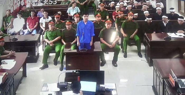 Bị cáo mặc áo xanh đứng tại vị trí xét hỏi trong phiên tòa.