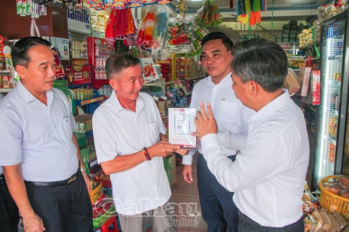 Ông Huỳnh Huy Phong, chủ Tiệm tạp hoá Phong Liên (thứ hai từ trái sang), được hướng dẫn sử dụng mã QR trong thanh toán.
