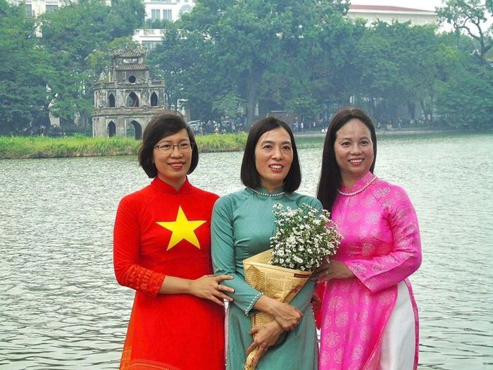Bên hồ Hoàn Kiếm, chị em phụ nữ diện áo dài với những gam màu nổi bật cùng nhau tạo dáng chụp ảnh, phía sau là Tháp Rùa cổ kính.
