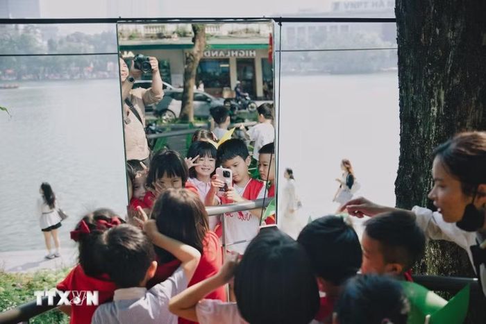 Các em nhỏ hào hứng chụp ảnh lưu niệm qua hệ thống gương nghệ thuật tại không gian “Dải lụa ký ức” bên hồ Hoàn Kiếm trong dịp kỷ niệm 72 năm Ngày Giải phóng Thủ đô. (Ảnh: Phạm Tuấn Anh/TTXVN)