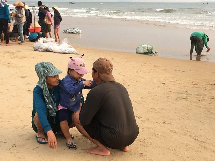 Một khoảng lặng giữa phiên chợ: Người lớn trò chuyện, em bé vui mừng đón cha trở về sau chuyến biển đêm, hoạt động mua bán vẫn diễn ra phía sau