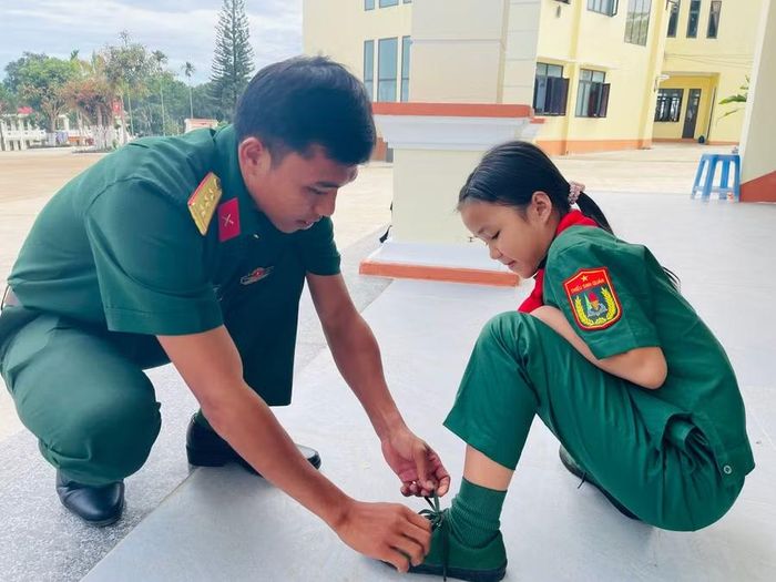 Thượng úy So Minh Sự - giáo viên Khoa Quân sự kiêm lớp trưởng lớp 6/2 buộc lại dây giày cho em Sô Thị Ánh Dương. Ảnh: P.D