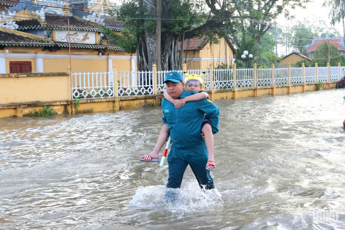Không ngại lội nước, lực lượng dân quân tận tình đưa học sinh Trường Tiểu học Bình Thủy qua đoạn đường ngập, vào lớp an toàn.