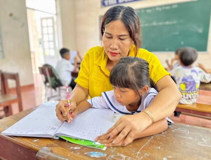  Giáo viên Trường Tiểu học Vân Canh - điểm làng Canh Giao (phân hiệu 2) hướng dẫn học sinh lớp 1 tập viết. Ảnh: C.H 
