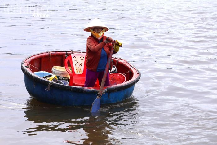Một người phụ nữ chèo thuyền thúng đi thu mua cá.