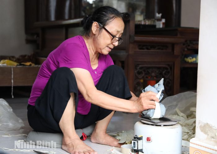 Người thợ dùng miếng gang nóng là phẳng từng tàu lá, giúp lá giữ được độ phẳng, mềm và màu sắc tự nhiên.