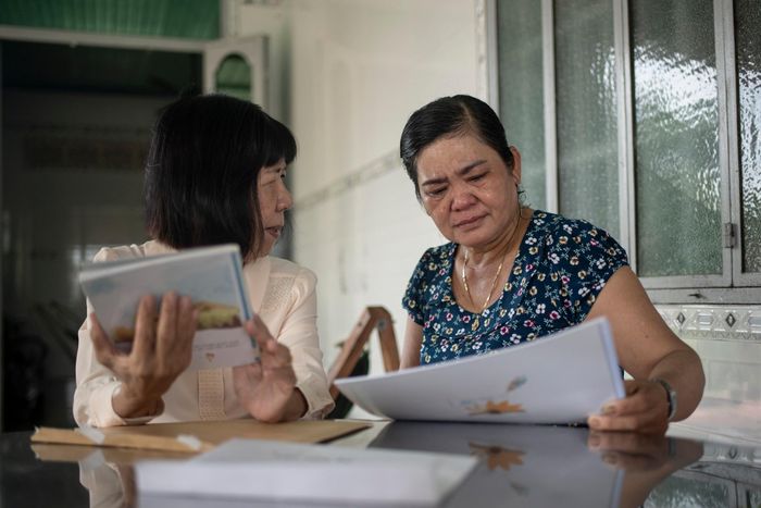  Cô Đinh Thị Kim Phấn (áo trắng, 70 tuổi) có quãng thời gian hơn 17 năm dạy học cho bệnh nhi ung thư tại TP.HCM. Tháng 7/2026, cô đến gia đình chị Bùi Thị Nhen (Tây Ninh) để trao lại cho chị cuốn vở của con gái chị, bé Đặng Thùy Trâm. 