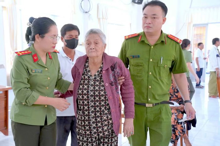 Cán bộ Công an xã Tân Tiến, tỉnh Cà Mau hỗ trợ thân nhân liệt sĩ già yếu đến điểm thu nhận sinh phẩm ADN. (ảnh HỮU ĐỆ).