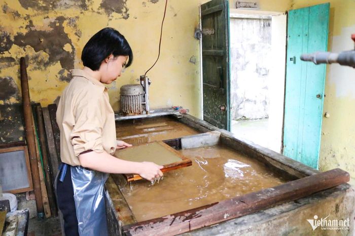 Giữa xưởng nhỏ thoang thoảng mùi vỏ dó, đôi tay chị Huyền miệt mài bên bể bột, thoăn thoắt xeo từng tờ giấy mỏng nhẹ