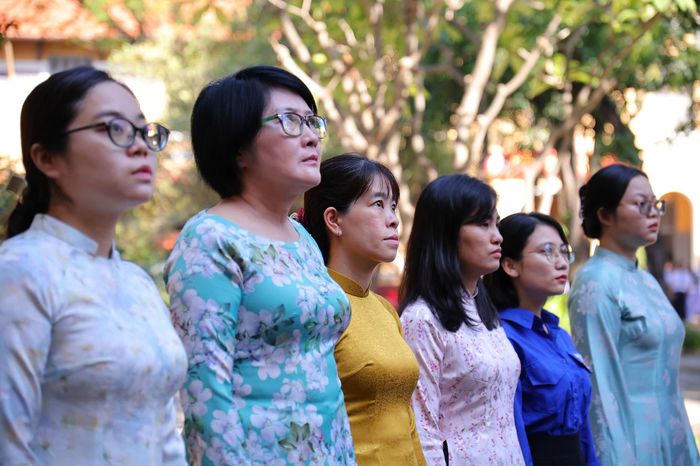  Để học sinh có cơ hội trực tiếp bày tỏ lòng tri ân, trường THPT Nguyễn Thị Minh Khai huy động khoảng 300 học sinh cùng 5 giáo viên tổ Lịch sử, đại diện ban giám hiệu và Đoàn trường tham gia lễ tiễn đưa. Trao đổi với Tri Thức - Znews, cô Nguyễn Thị Hồng Chương, Hiệu trưởng nhà trường, cho biết thầy cô và học sinh đã chuẩn bị cờ, hoa từ sớm cho hoạt động ý nghĩa này. Đồng thời nhắc nhở các em giữ thái độ nghiêm túc, trật tự trong suốt buổi lễ. Ảnh: Võ Kỳ. 