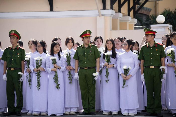  Đúng 8h30, dưới sự hướng dẫn của nhà trường và lực lượng Công an TP.HCM, 300 học sinh trường THPT Nguyễn Thị Minh Khai lần lượt di chuyển ra đường Điện Biên Phủ. Các em đứng thành hàng ngay ngắn, tay cầm hoa trắng và cờ Tổ quốc, hướng mắt về phía đoàn xe sẽ đi qua.