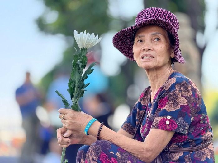 Một người dân cầm nhành hoa cúc trắng chờ đoàn xe đưa tiễn các anh hùng liệt sĩ. Ảnh: Hoàng Hải
