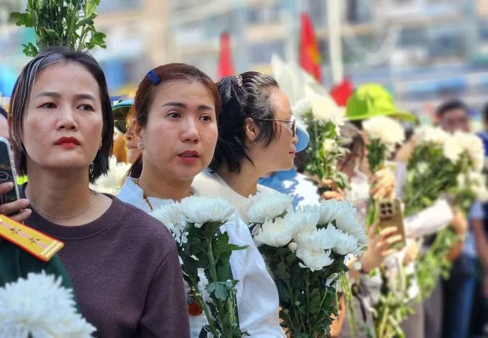 Người dưng cầm hoa trắng đứng hai bên đường đoàn xe đi qua.