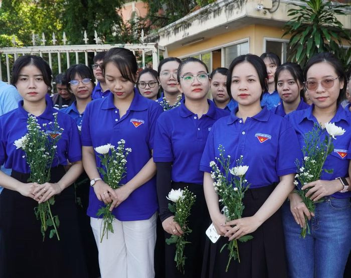 Đoàn viên thanh niên cầm hoa cúc trắng và hoa thạch thảo đứng chờ đoàn xe tại vòng xoay Điện Biên Phủ.