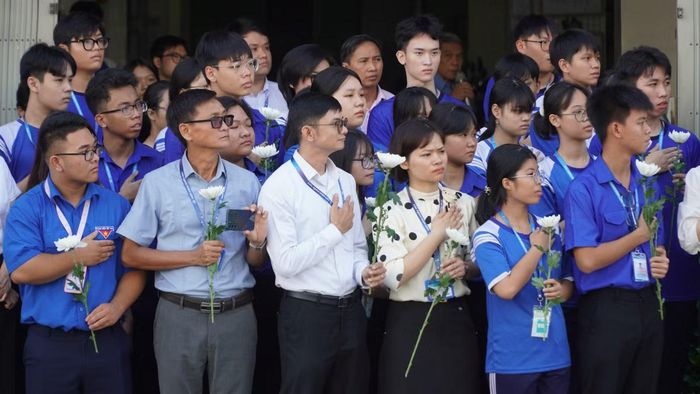 Ban giám hiệu và học sinh lớp 12 Trường THPT Năng khiếu Thể dục Thể thao TPHCM đồng loạt đặt tay phải lên ngực trái, tay còn lại cầm hoa cúc trắng.