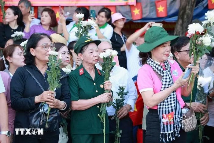 Người dân cầm hoa chờ tiễn đoàn xe đưa liệt sỹ. (Ảnh: Mạnh Minh/TTXVN)
