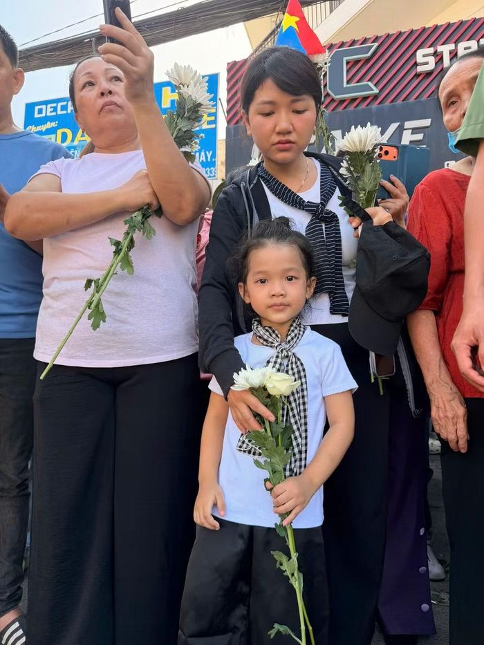 Một em bé theo mẹ xếp hàng tiễn đoàn xe chở hài cốt liệt sĩ đi qua. (Ảnh: PV/Vietnam+)