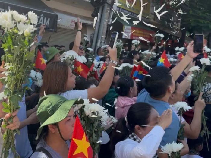 Người dân xúc động, vừa hát Quốc ca vừa giơ cao tay chào, tiễn biệt các anh. (Ảnh: PV/Vietnam+)