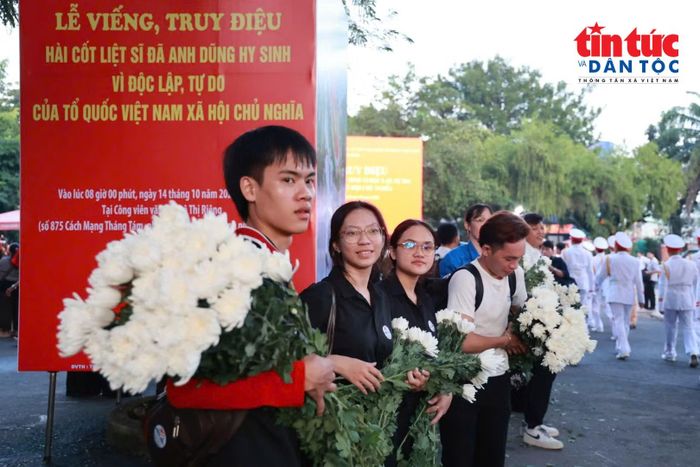 Người dân cầm hoa trắng chờ tiễn các liệt sĩ trước cổng Công viên Lê Thị Riêng sáng 14/10.
