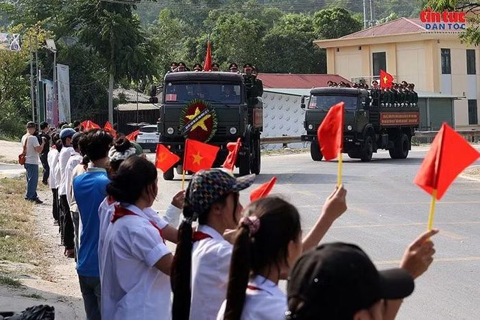 Người dân và các em học sinh cầm cờ Tổ quốc, đứng hai bên đường thành kính đón đoàn xe đưa hài cốt liệt sĩ .