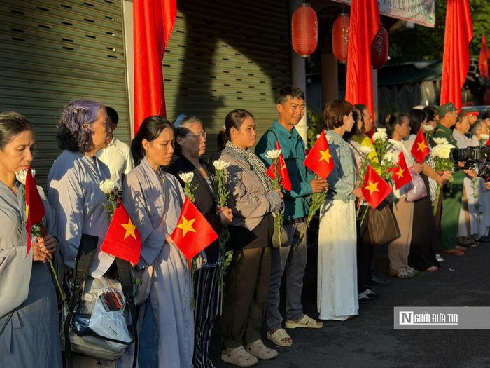 Trên tay mỗi người dân là 1 cành hoa cúc trắng và lá cờ đỏ sao vàng. (Ảnh: Mỹ Hậu)