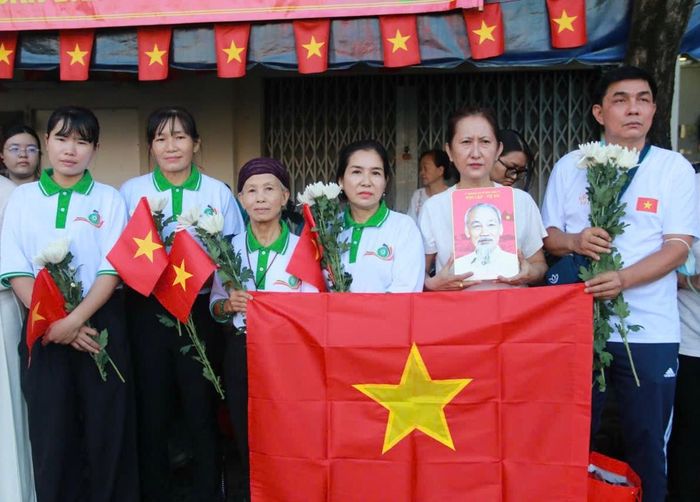 Người dân với cờ Tổ quốc, ảnh Bác Hồ và hoa trắng trên tay tiễn đưa các liệt sĩ