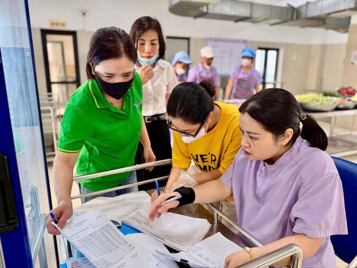 Đại diện nhà cung cấp, các cô giáo và phụ huynh học sinh Trường Mầm non Phúc Lợi ký cân, bàn giao số lượng thức ăn được nấu trong ngày 14-10. Ảnh: Ngọc Quỳnh