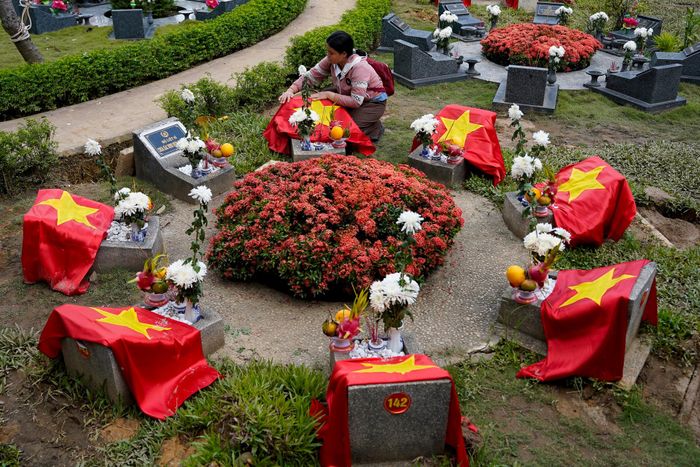  Một người dân thành kính chỉnh lại lá cờ Tổ quốc trên phần mộ liệt sĩ. Mỗi tấm bia được đánh số theo thứ tự được lực lượng chức năng tìm thấy, quy tập tại Công viên Lê Thị Riêng. Đằng sau đó là một cái tên, một danh tính liệt sĩ chờ được tìm lại để trở về với gia đình, quê hương. 