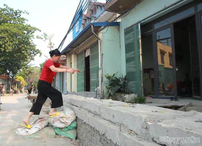 Bà Nguyễn Thị Việt, người dân thôn Nhân Chính, phải dùng các bao tải cát làm bậc tạm để bước qua đoạn cống bê tông cao khoảng 1m trước cửa nhà.