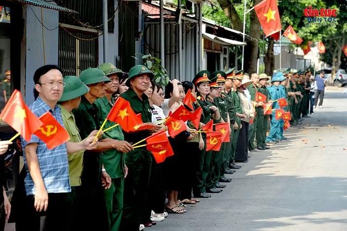Đông đảo người dân, cựu chiến binh và các lực lượng đứng dọc hai bên đường, cầm cờ Tổ quốc và cờ Đảng, thành kính chờ đón đoàn xe chở 93 hài cốt liệt sĩ trở về Nghĩa trang Liệt sĩ Quốc gia Vị Xuyên. Ảnh: Lê Phú