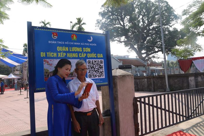 Bí thư Đoàn Thanh niên xã Phú Nghĩa Nguyễn Thị Thanh Hải hướng dẫn ông Trịnh Xuân Tựa, người dân thôn Lương Sơn tham quan di tích bằng điện thoại. Ảnh: Kim Nhuệ