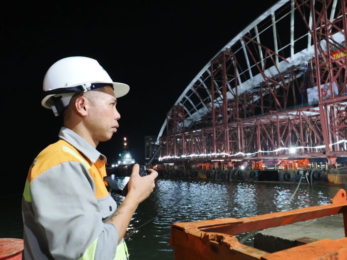  Kỹ sư sử dụng bộ đàm phối hợp điều hành quá trình đưa kết cấu cầu lên sà lan. Ảnh: HOÀNG HÙNG 
