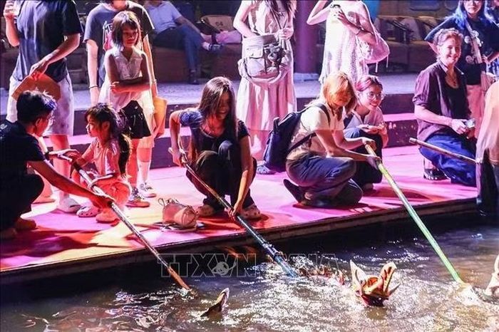 Khán giả trải nghiệm trực tiếp điều khiển con rối dưới sự hướng dẫn của các nghệ nhân múa rối nước. Ảnh: Khánh Hoà/TTXVN