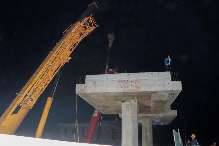 Tại công trường, nhà thầu bố trí các cẩu chuyên dụng đảm nhận nhiệm vụ nâng dầm. Khi mọi khâu chuẩn bị hoàn tất, hai cẩu phối hợp nâng cấu kiện khỏi xe vận chuyển, từng bước đưa phiến dầm lên khỏi mặt sàn xe.