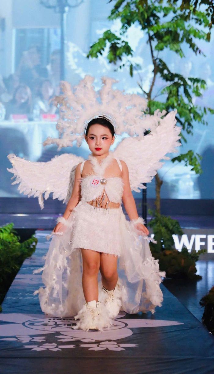 Người mẫu nhí tự tin trình diễn trang phục thiên thần màu trắng với thiết kế cánh lông vũ cầu kỳ, tạo điểm nhấn nổi bật trên sàn diễn Chung kết Vietkids Junior Fashion Week.