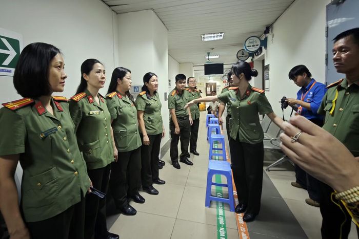 Cán bộ Phòng Tổ chức cán bộ - CATP Hà Nội đứng dọc hành lang nghe phân công, hàng ghế nhựa xanh theo vạch sơn để làm sao tạo thuận lợi nhất cho người hiến tóc